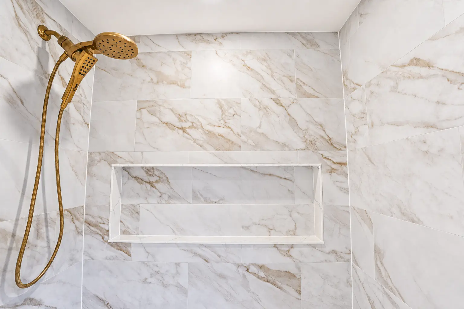 Marble-tiled shower with recessed niche and brass rain head