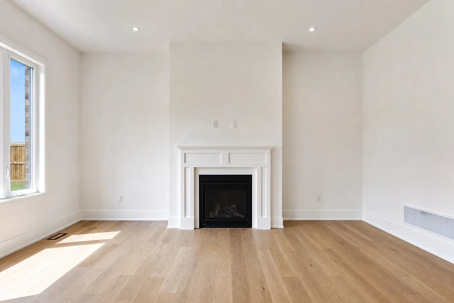 Living room with panelled gas fireplace and oak floors